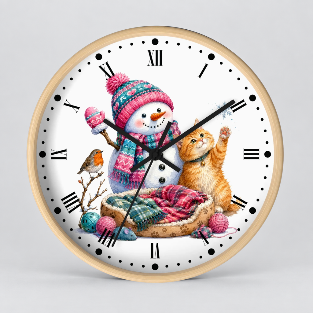 A round wall clock with a light wood frame and a white face, decorated with a festive winter illustration featuring a snowman in a pink knit hat, an orange tabby cat, a small bird, and colorful yarn balls. The clock is centered against a neutral light gray background.