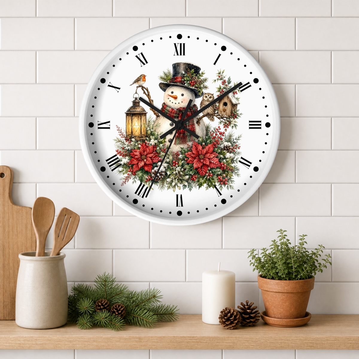 A round white wall clock with a festive Christmas design featuring a snowman, red poinsettias, a bird, and a owl. The clock is mounted on a white subway tile wall above a wooden shelf styled with kitchen utensils, pine branches, a candle, and a potted plant.