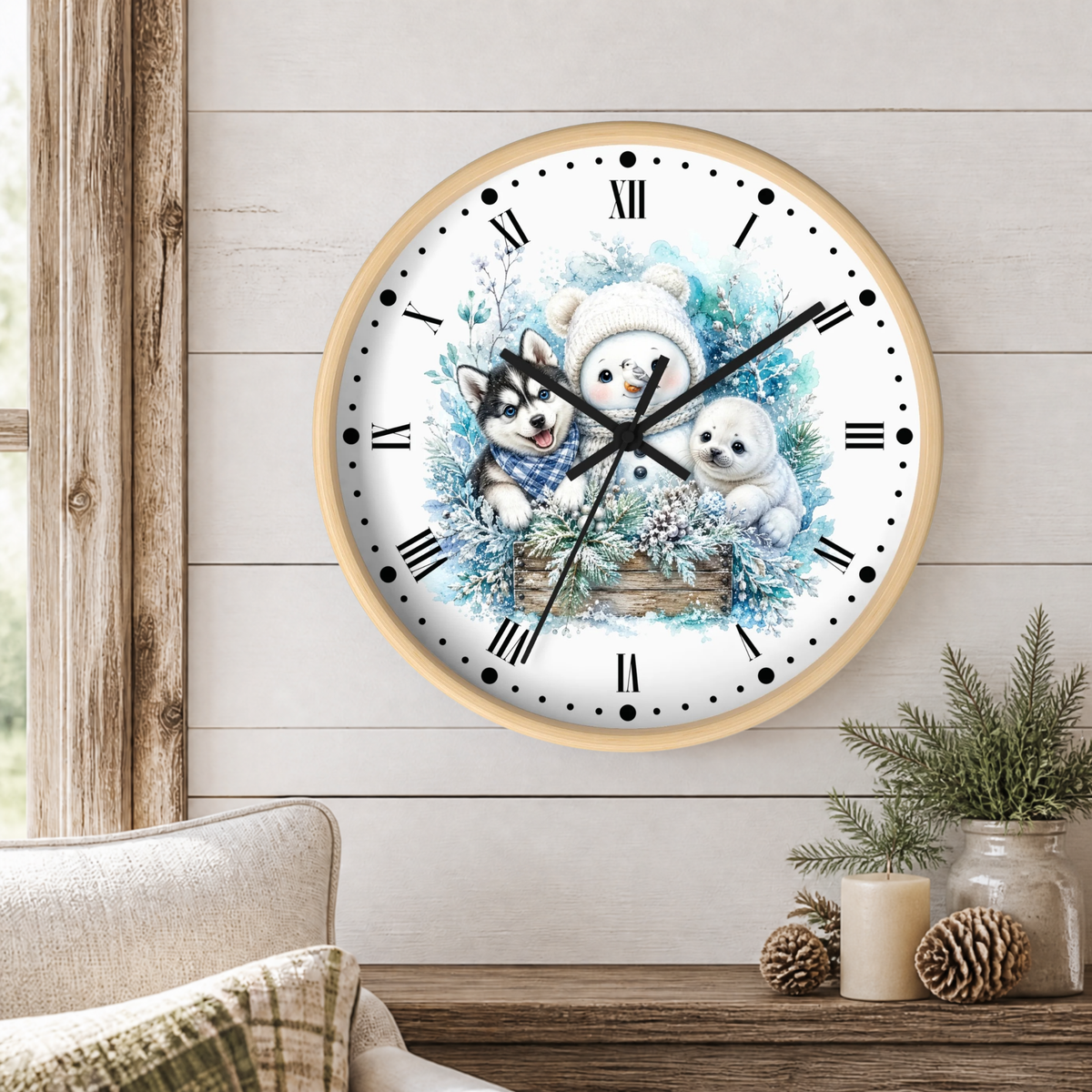 A round wall clock with a light wood frame hangs on a white shiplap wall above a wooden table. The clock face features a winter illustration of a snowman, a husky, a puppy, and blue floral accents.