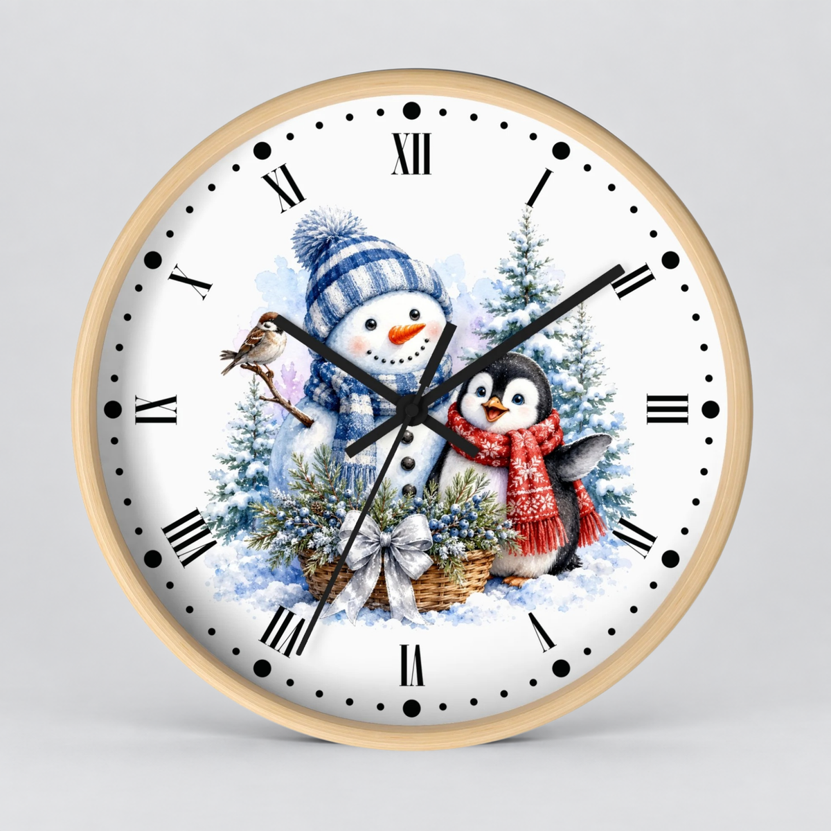 A round wall clock with a light wood frame and a white face featuring a winter holiday illustration of a snowman and penguin among snowy trees. The clock has black Roman numerals, black hands, and is photographed against a neutral light gray background.