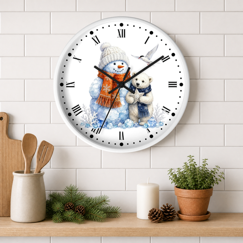 A round wall clock with a white face and black Roman numerals, featuring a winter illustration of a snowman in an orange scarf hugging a polar bear, displayed on a white subway tile wall above a wooden shelf with kitchen decor and a potted plant.