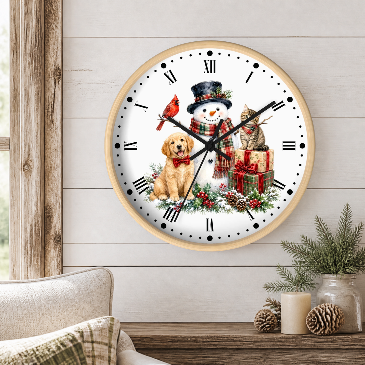 A round wall clock with a light wood frame hangs on a white shiplap wall above a wooden table. The clock face features a festive Christmas illustration with a snowman, golden retriever dog, red cardinal, ginger cat, wrapped gifts, pinecones, and holly.