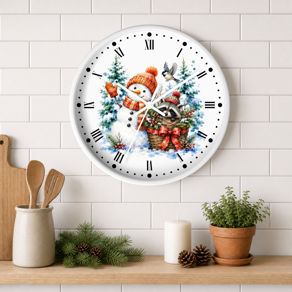 A round white wall clock with a festive winter illustration of a snowman, birds, evergreen trees, and a basket with red bows. The clock is mounted on a white subway tile wall above a wooden shelf styled with kitchen utensils, pine branches, a candle, and a potted plant.