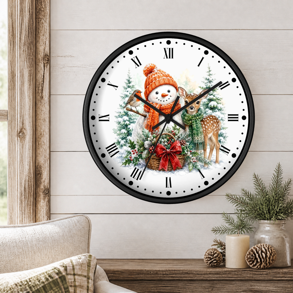 A round wall clock with a black frame and a festive winter illustration on the face, hanging on a light wood paneled wall above a wooden table with candles and greenery.