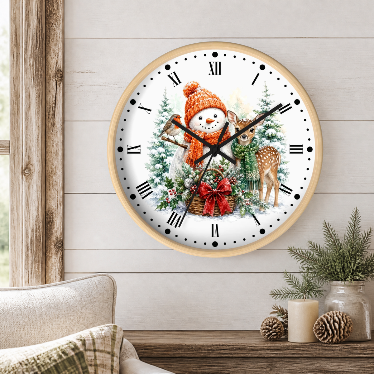 A round wall clock with a light wood frame hangs on a white shiplap wall above a wooden table. The clock face features a festive winter illustration with a snowman in an orange knit hat, a deer, a small tree, and a red gift box.