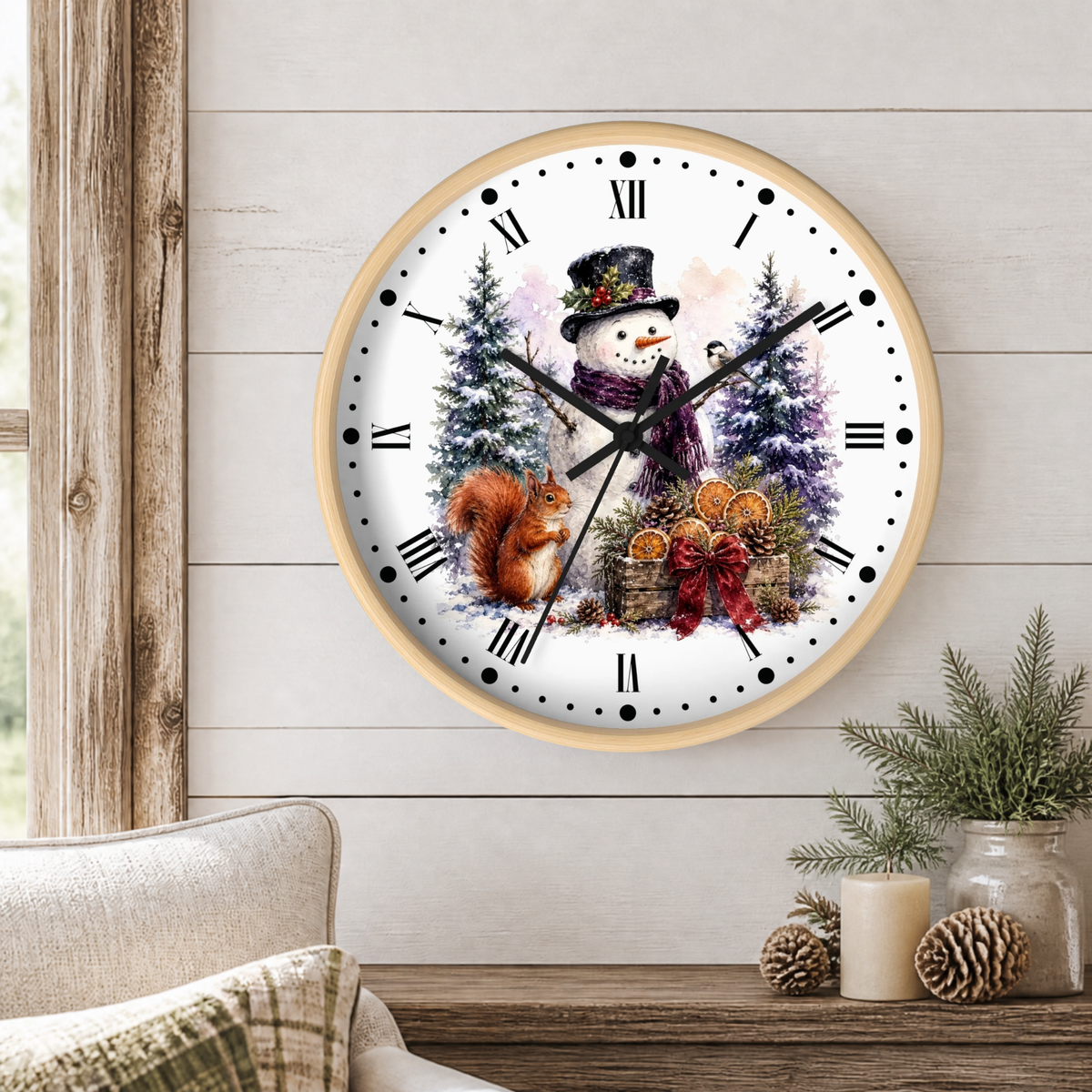 A round wall clock with a light wood frame hangs on a white shiplap wall above a rustic wooden table. The clock face features a winter illustration with a snowman in a top hat, a red squirrel, evergreen trees, and a basket of ornaments.