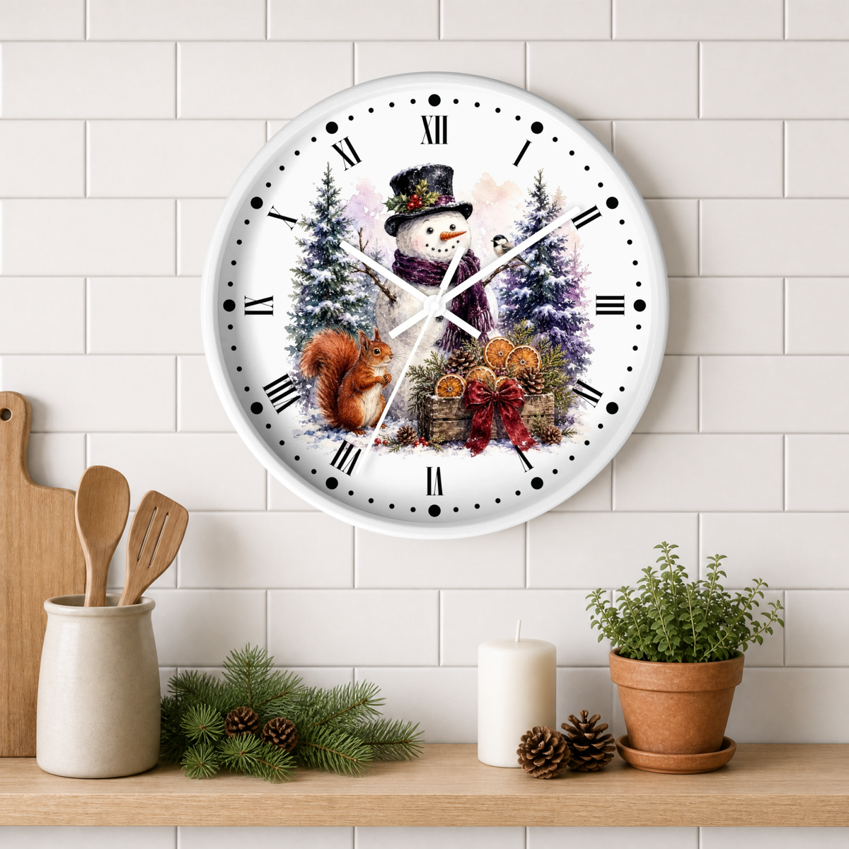A round white wall clock with a festive winter illustration of a snowman, trees, a squirrel, and pumpkins, styled on a wooden shelf against a white subway tile wall.