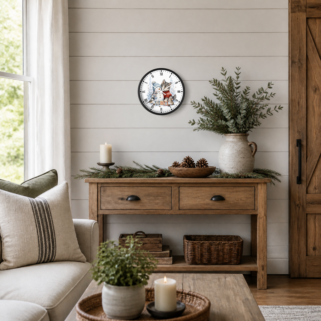 A round wall clock with a colorful winter snowman in a blue knit hat and forest animals illustration hangs on a white shiplap wall above a rustic wooden console table styled with greenery, pinecones, and candles in a bright, cozy living room.