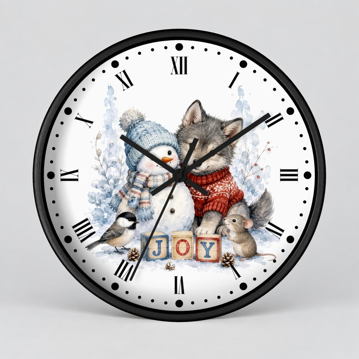 A round wall clock with a black frame and a white face featuring a winter illustration of a wolf, snowman, bird, and small mouse around wooden blocks spelling 'JOY'. The clock is shown against a light gray background.