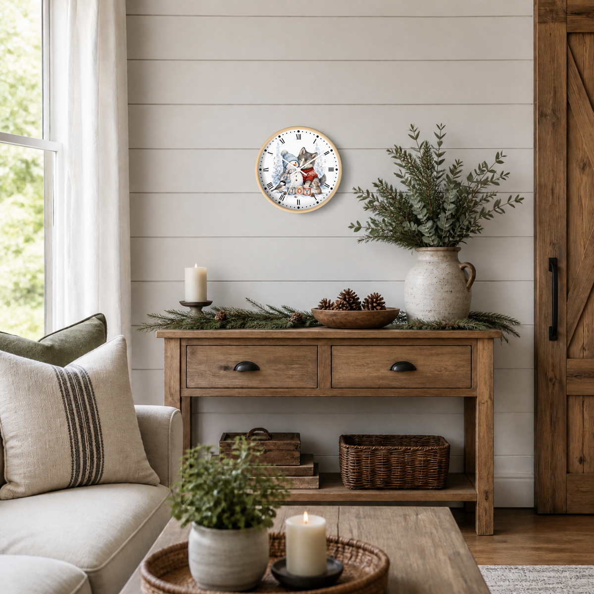 A round wall clock with a rustic illustration of a snowman & animal friends, styled in a cozy living room above a wooden console table with holiday greenery and a vase.