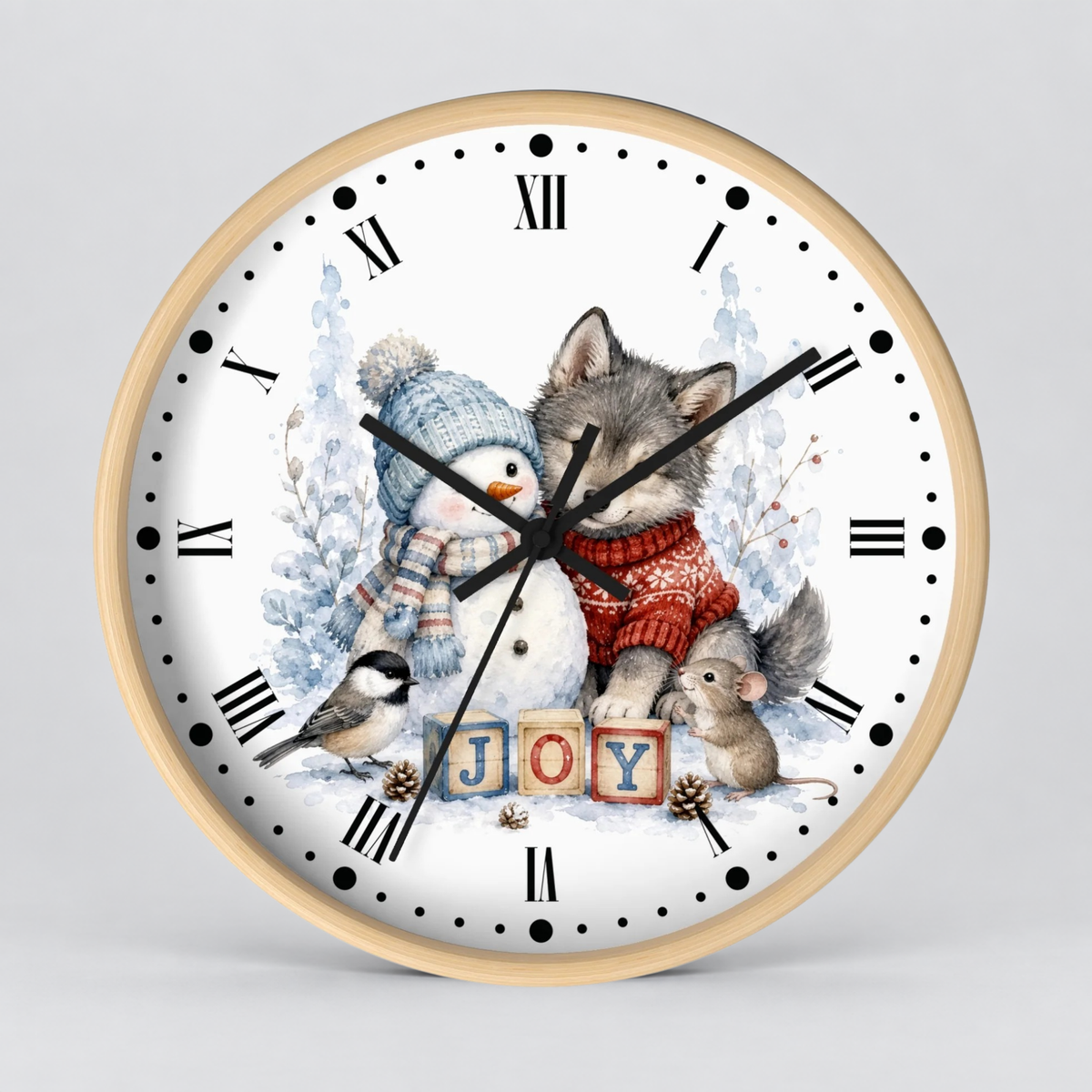 A round wall clock with a light wood frame and a white face, decorated with a winter holiday illustration featuring a gray wolf in a red sweater, a snowman, a bird, a mouse, and the word 'JOY' in wooden blocks. The clock is shown against a neutral light gray background.