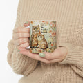 Person holding a mug with owl design and 'So Hooten Loved' text, wearing a beige sweater.