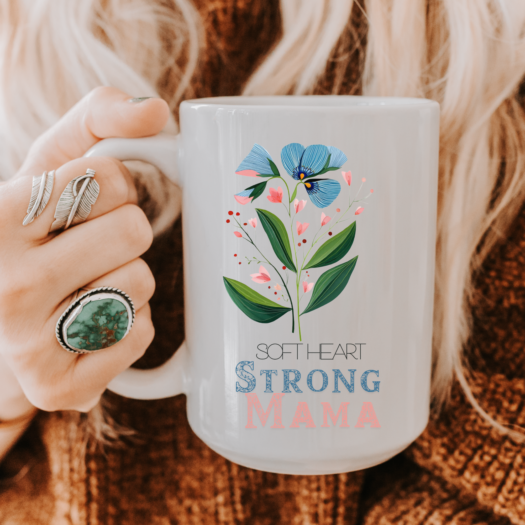 15oz white ceramic mug with floral design and text held by a person wearing rings, on a textured fabric background