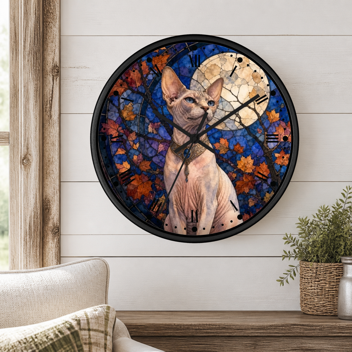 A round wall clock with a black frame featuring a Sphynx cat illustration over a stained-glass-style autumn leaf background, mounted on a white wood-paneled wall above a wooden shelf with a plant and part of a sofa visible.