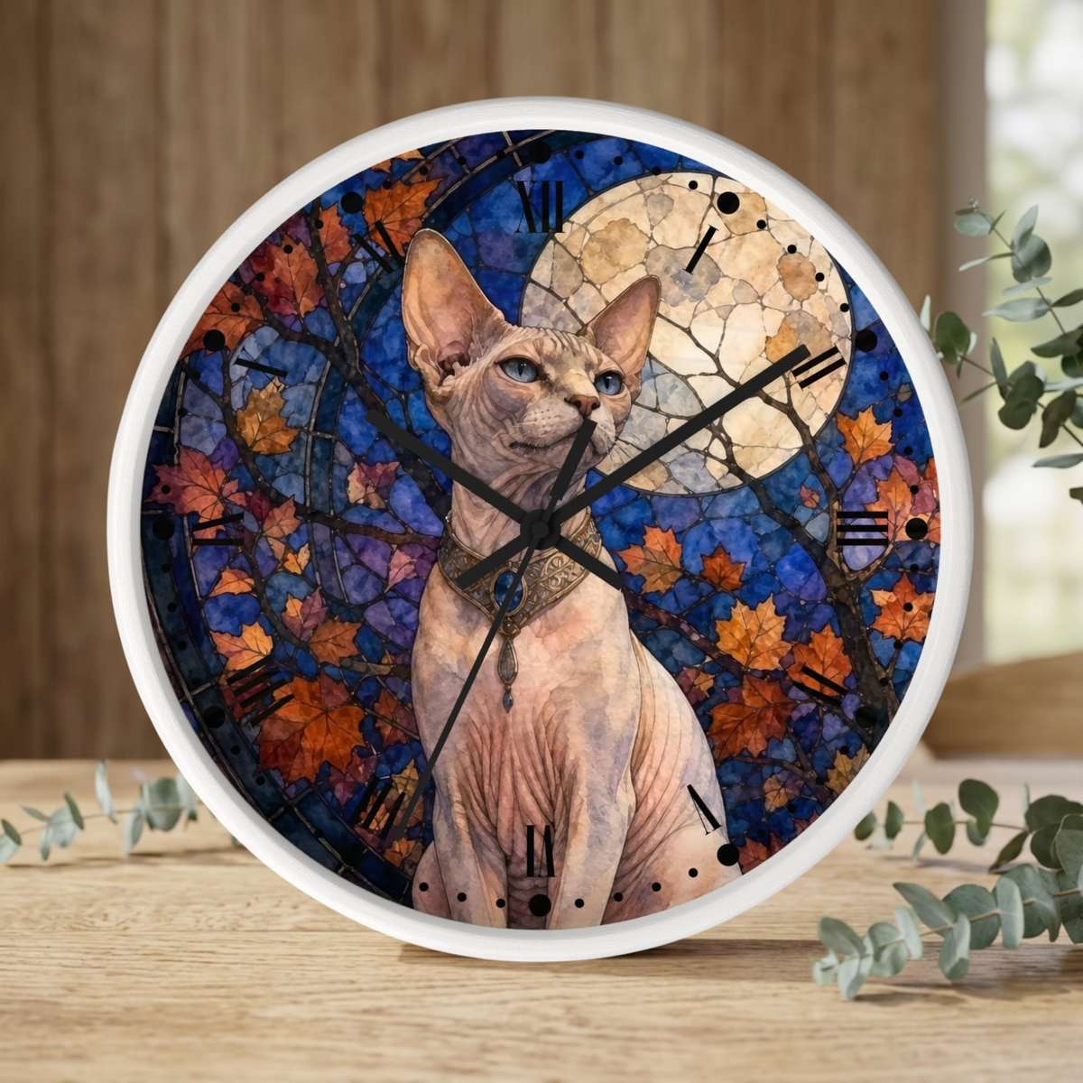 A round wall clock with a white frame, featuring a printed design of a hairless cat in front of a blue stained-glass-style background with autumn leaves and a moon. The clock is shown on a wooden surface with eucalyptus branches.