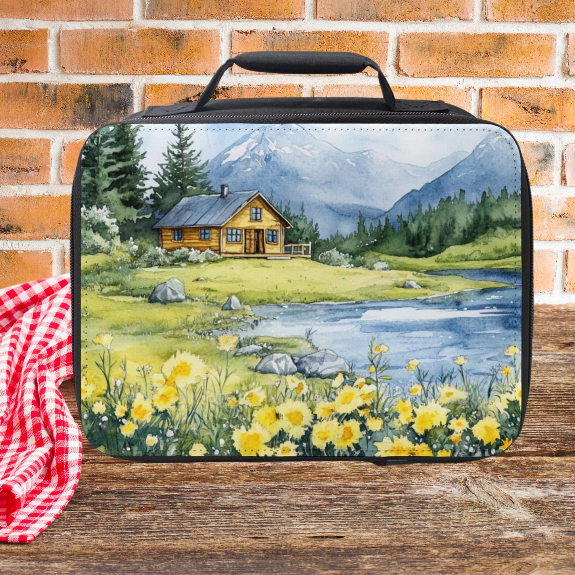  insulated lunch bag with nature scene of a cabin in the spring time design on a wooden picnic table against a brick wall background.