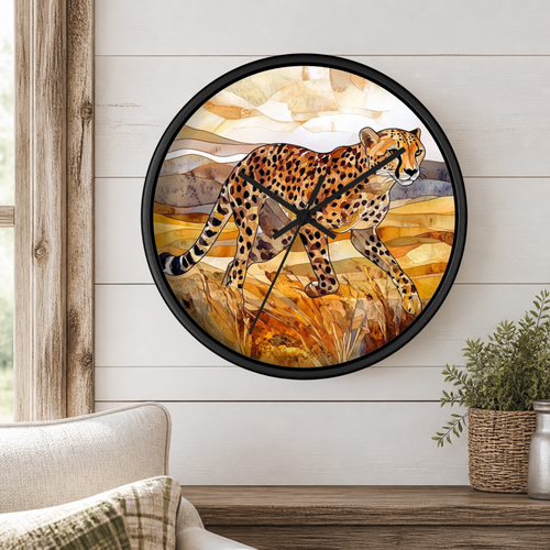 Round wall clock with a black frame featuring a watercolor-style cheetah walking through golden grass, mounted on a white shiplap wall above a wooden table with a potted plant.