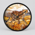Round wall clock with a black frame and black hands, featuring a watercolor-style illustration of a cheetah walking through golden grass against warm beige and brown landscape shapes.
