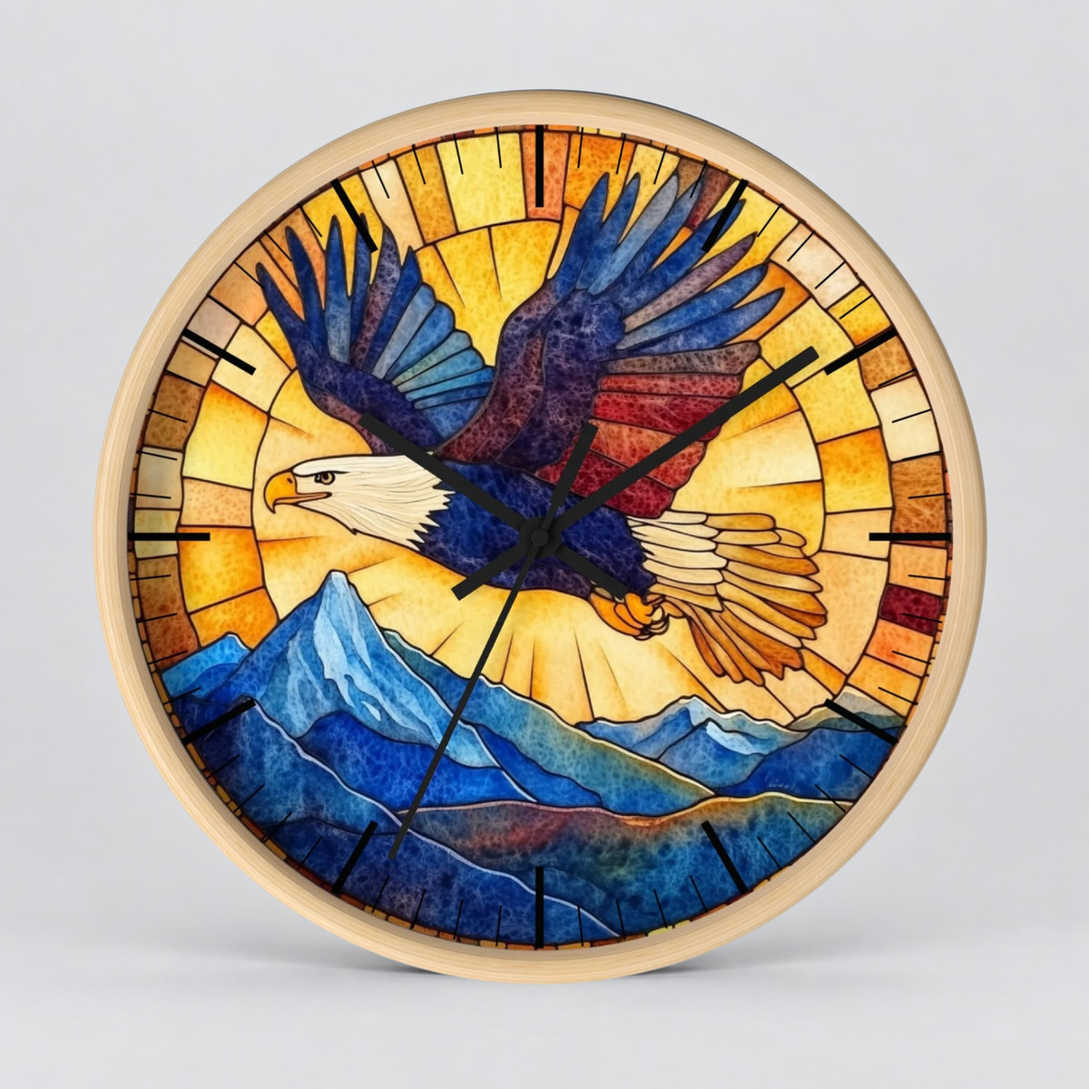 A round wall clock with a stained-glass-style design featuring a bald eagle flying over blue mountains, set in a light wood frame against a neutral gray background.