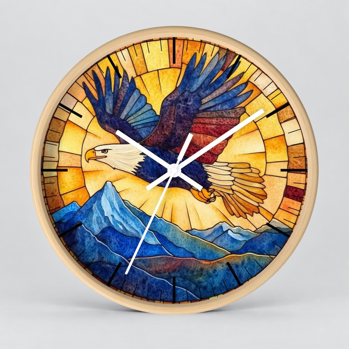 A round wall clock with a light natural wood frame, featuring a stained-glass-style illustration of a bald eagle flying over blue mountains against a warm yellow and orange sunburst background. The clock has white hands and black hour markers.