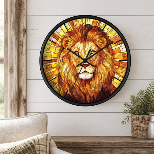 A round wall clock with a black frame and a stained-glass-style lion face design in warm yellow, orange, and brown tones, mounted on a white shiplap wall above a wooden surface with a small plant and part of a chair visible.