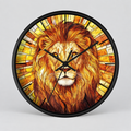 A round wall clock with a black frame featuring a stained-glass style illustration of a lion's face and golden rays. The clock is shown against a neutral light gray background.