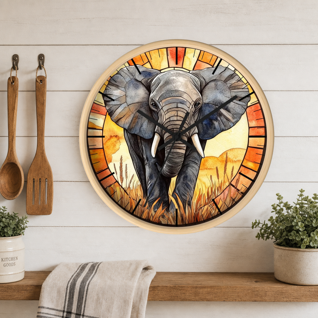 A round wall clock featuring a stained-glass-style illustration of an elephant in warm orange, yellow, and red tones, mounted on a white wood plank wall above a wooden shelf with plants and kitchen utensils.
