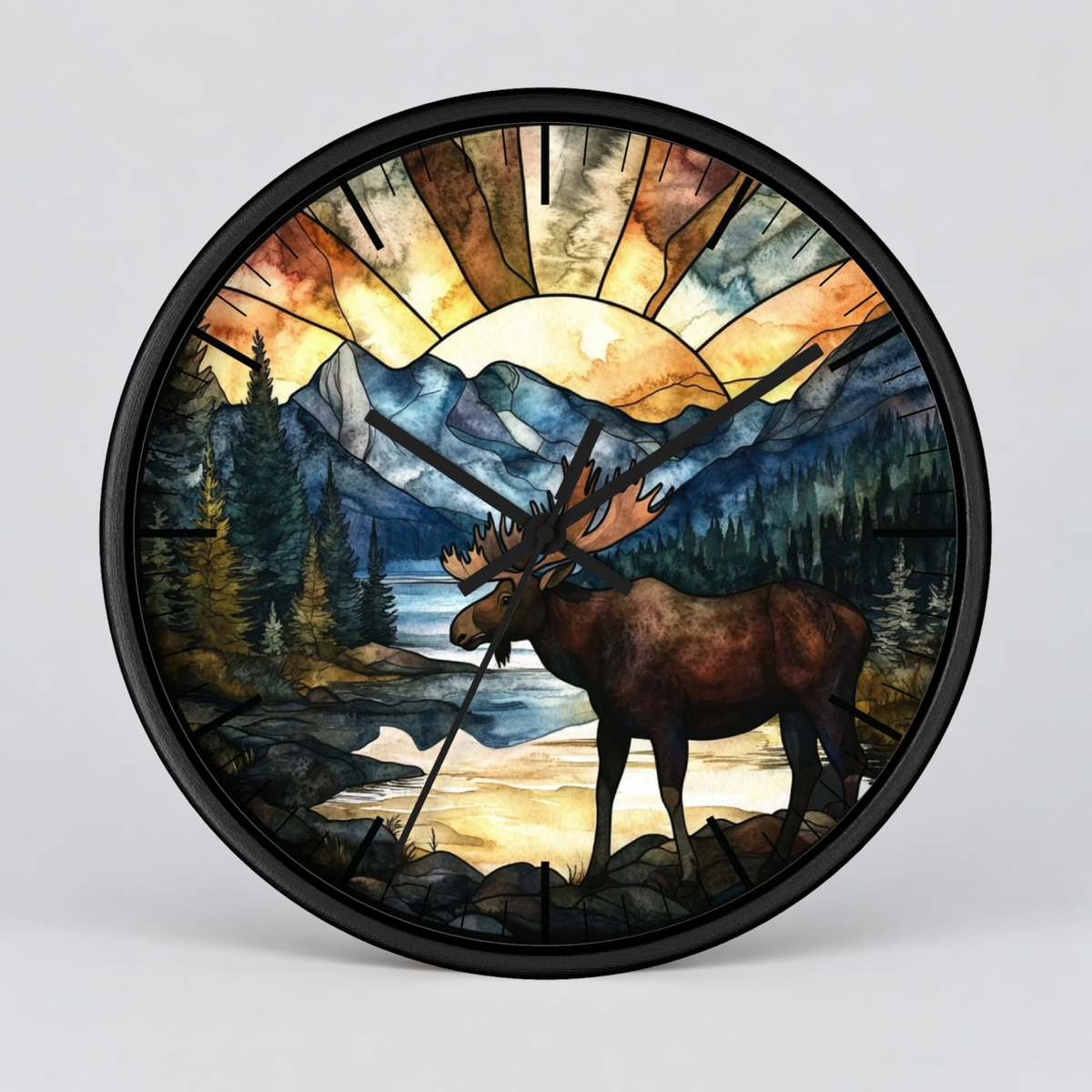 A round wall clock with a black frame and a stained-glass-style nature illustration featuring a moose, mountains, trees, and a glowing sun on a light gray background.
