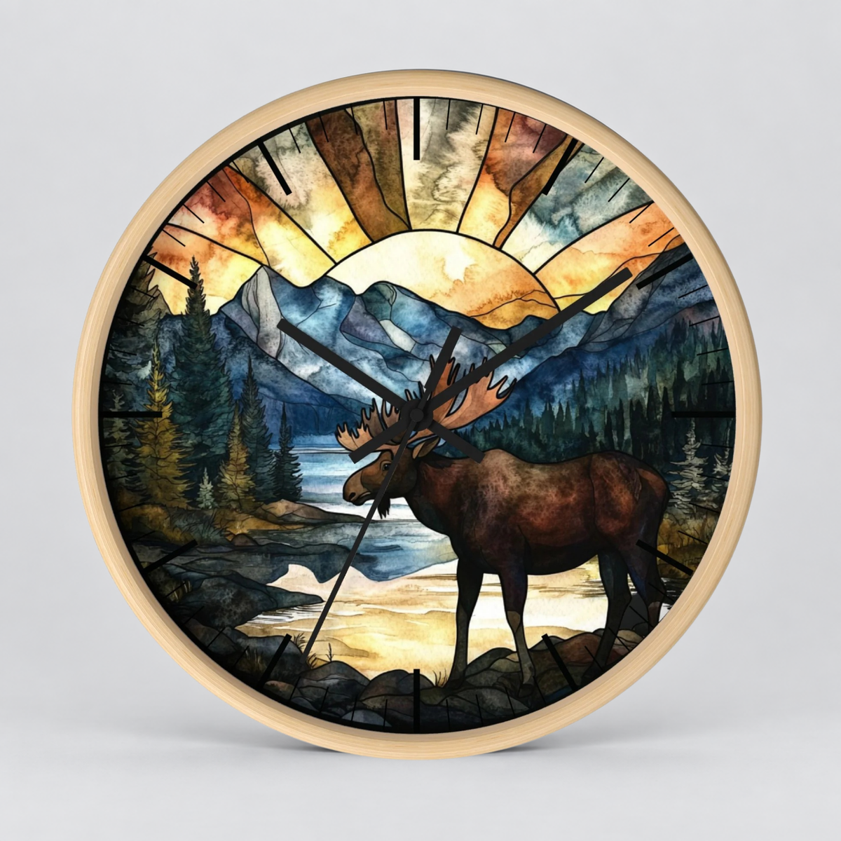 Round wall clock with a light wood frame and a stained-glass-style nature illustration featuring a moose, mountains, trees, and a sunburst, shown on a light gray background.
