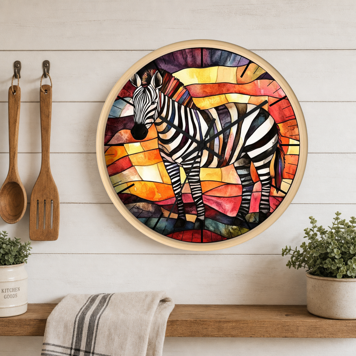 A round wall clock with a colorful stained-glass-style zebra illustration, mounted on a white wood plank wall above a wooden shelf with kitchen utensils, plants, and a towel.