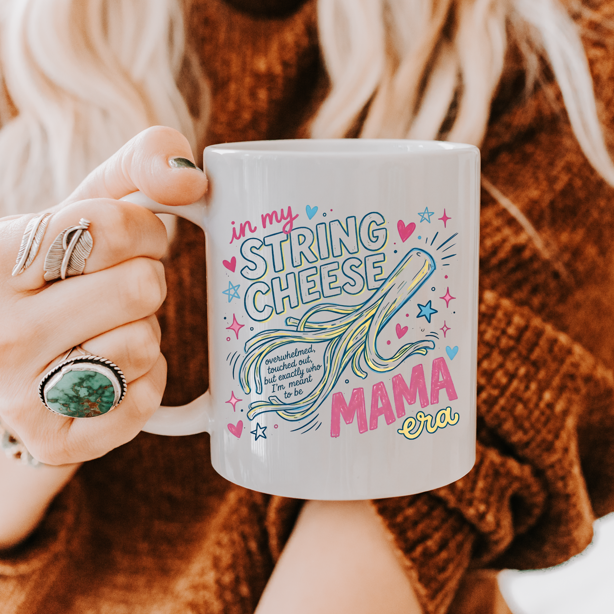 Person holding a mug with colorful text and graphics, wearing a brown sweater.
