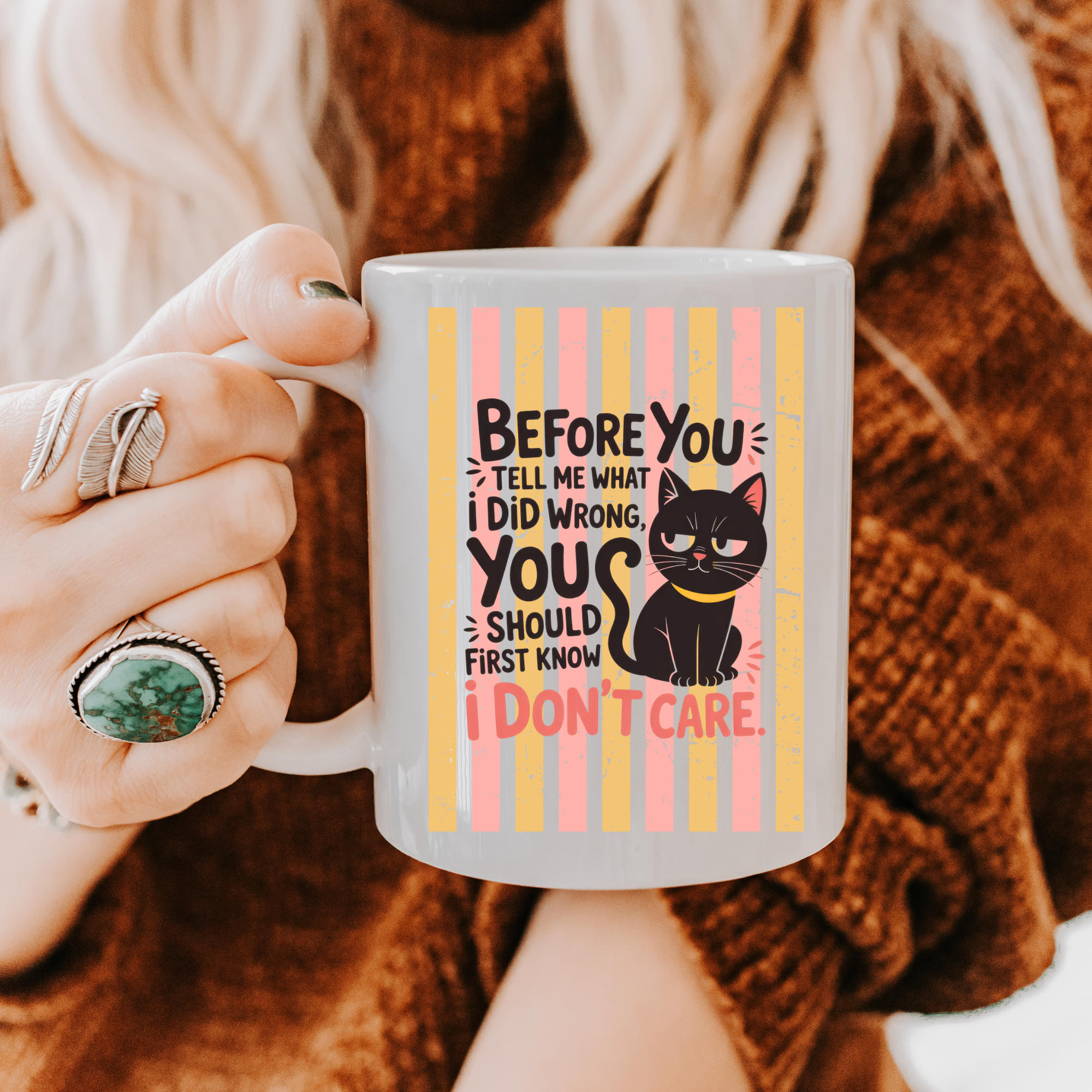 Person holding a 11oz mug with a black cat graphic and text, wearing a brown sweater.