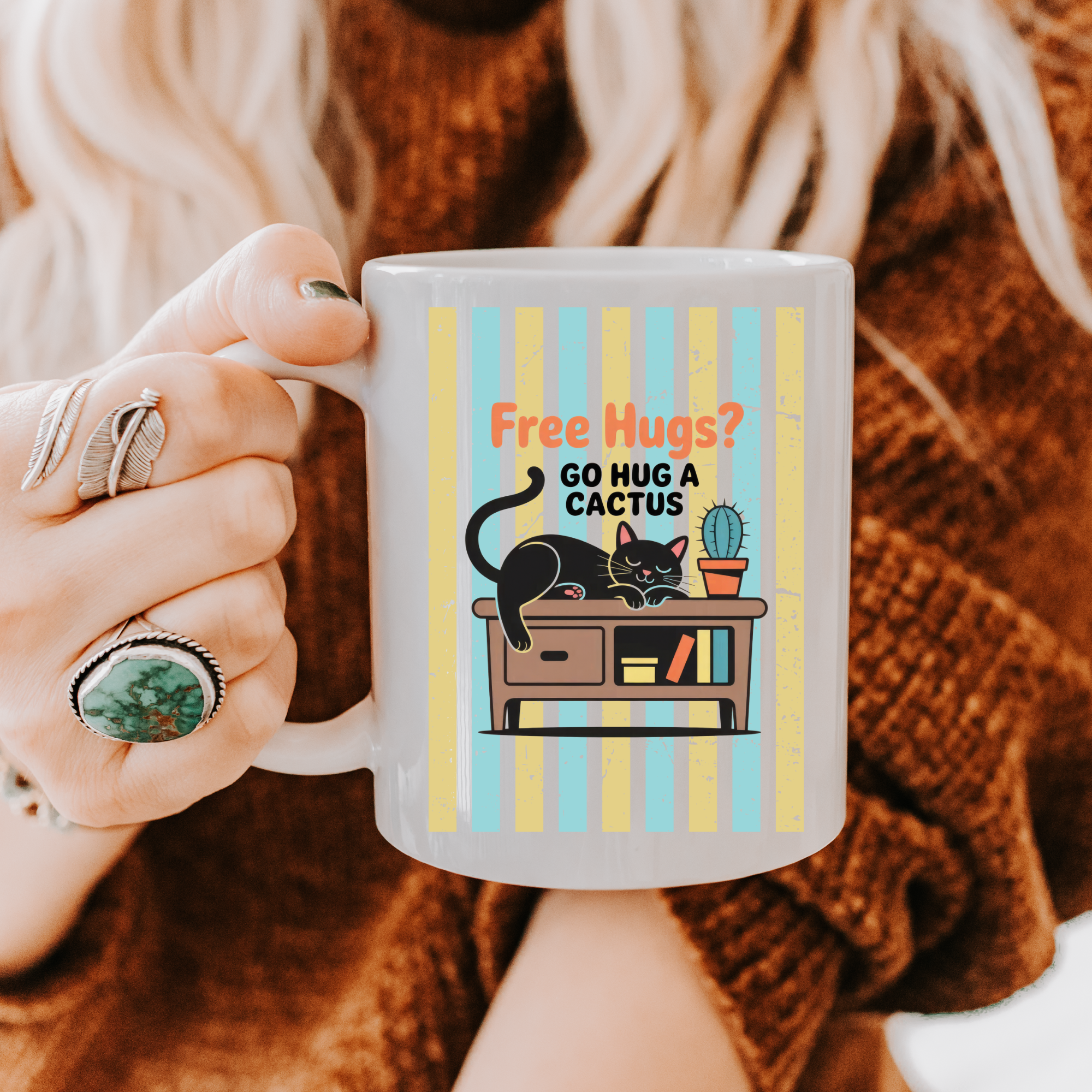 Person holding a 11oz mug with a cat and cactus illustration and text 'Free Hugs? Go hug a cactus'.