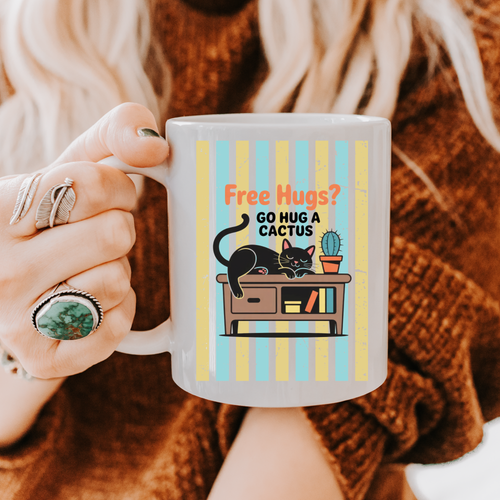 Person holding a 11oz mug with a cat and cactus illustration and text 'Free Hugs? Go hug a cactus'.