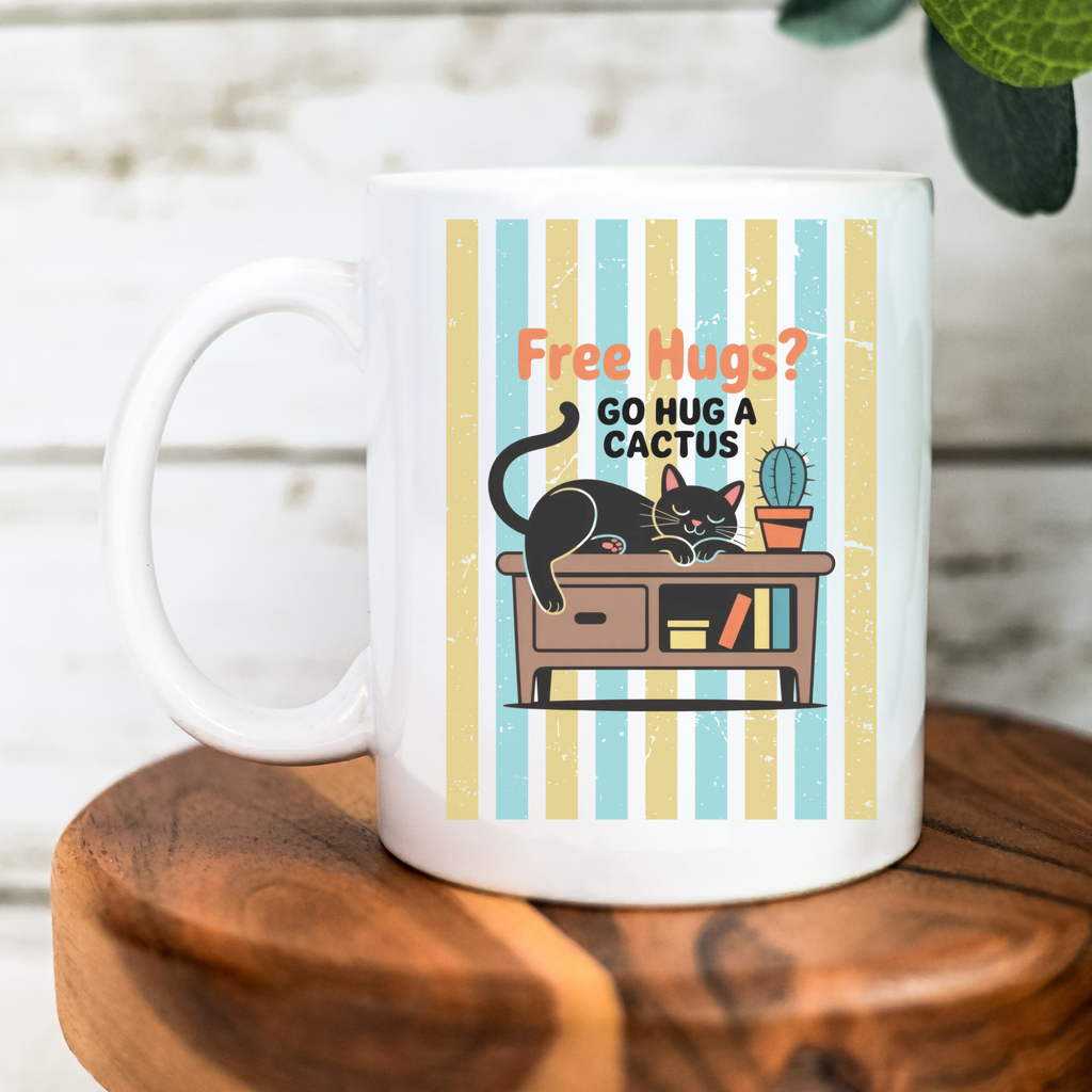 White 11oz mug with a cat and cactus design and text 'Free Hugs? Go Hug a Cactus' on a wooden surface.