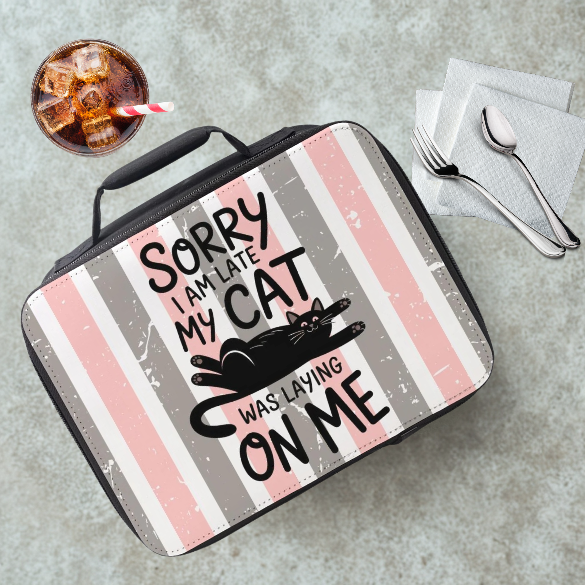 Lunch bag with a cat-themed design and text on a cafeteria table with a drink and utensils.