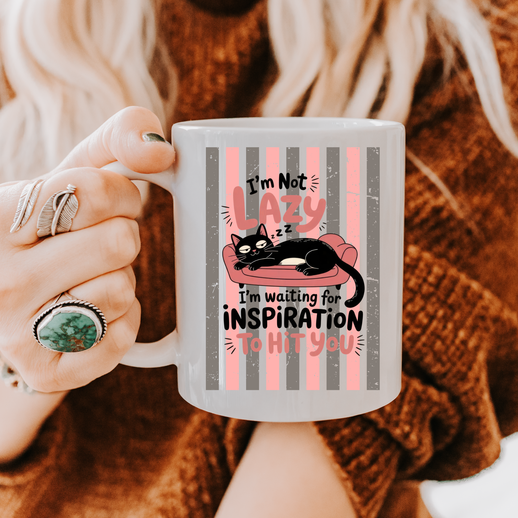 Person holding a 11oz mug with a cat design and text, wearing a brown sweater.