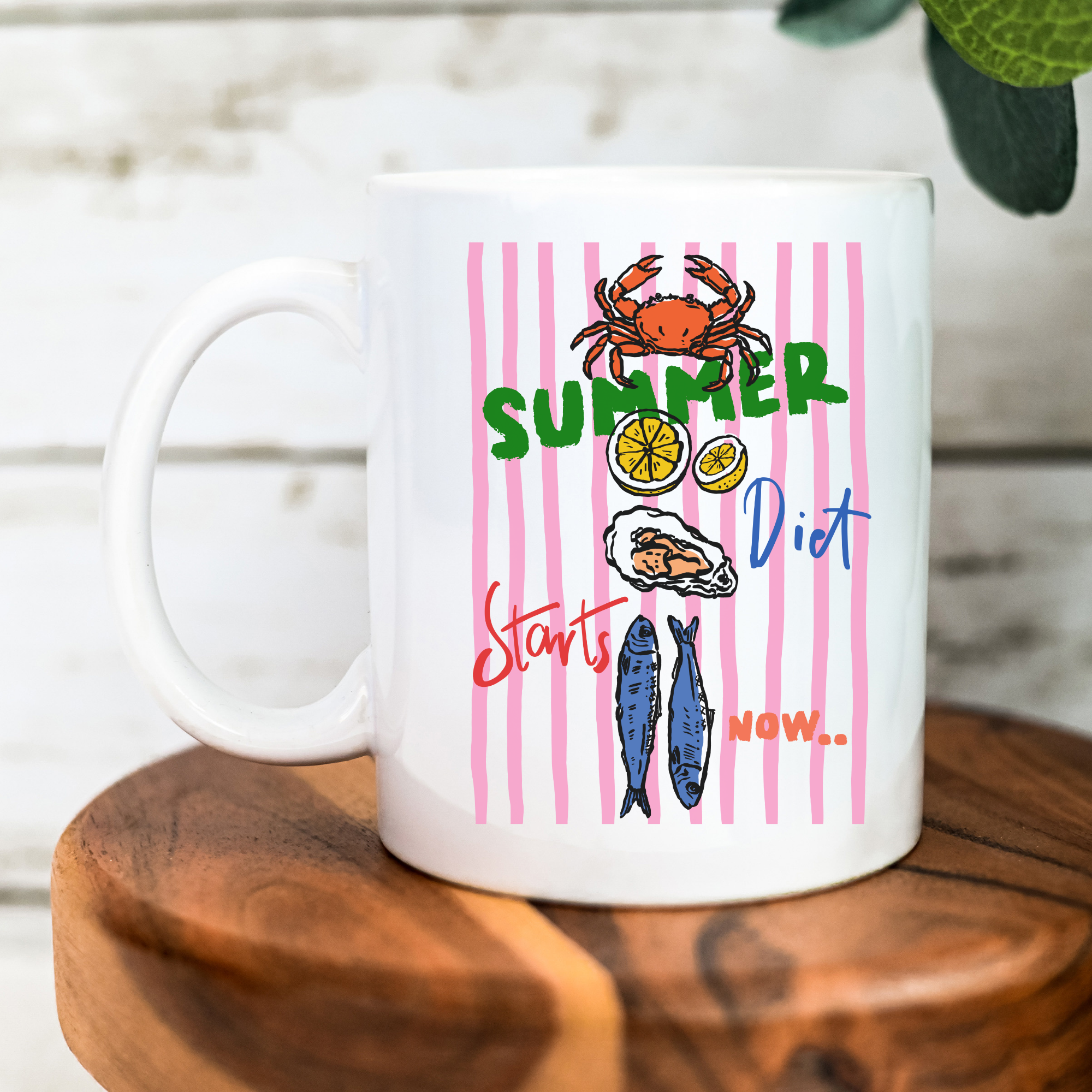 White 11oz. mug with summer-themed design featuring a crab, lemon, fish, and oyster on a pink striped background.
