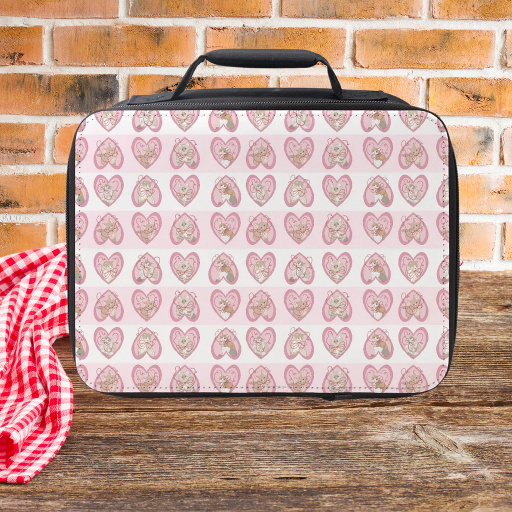 Lunch bag with hand drawn cats in pink hearts pattern on a wooden picnic table with a brick wall background