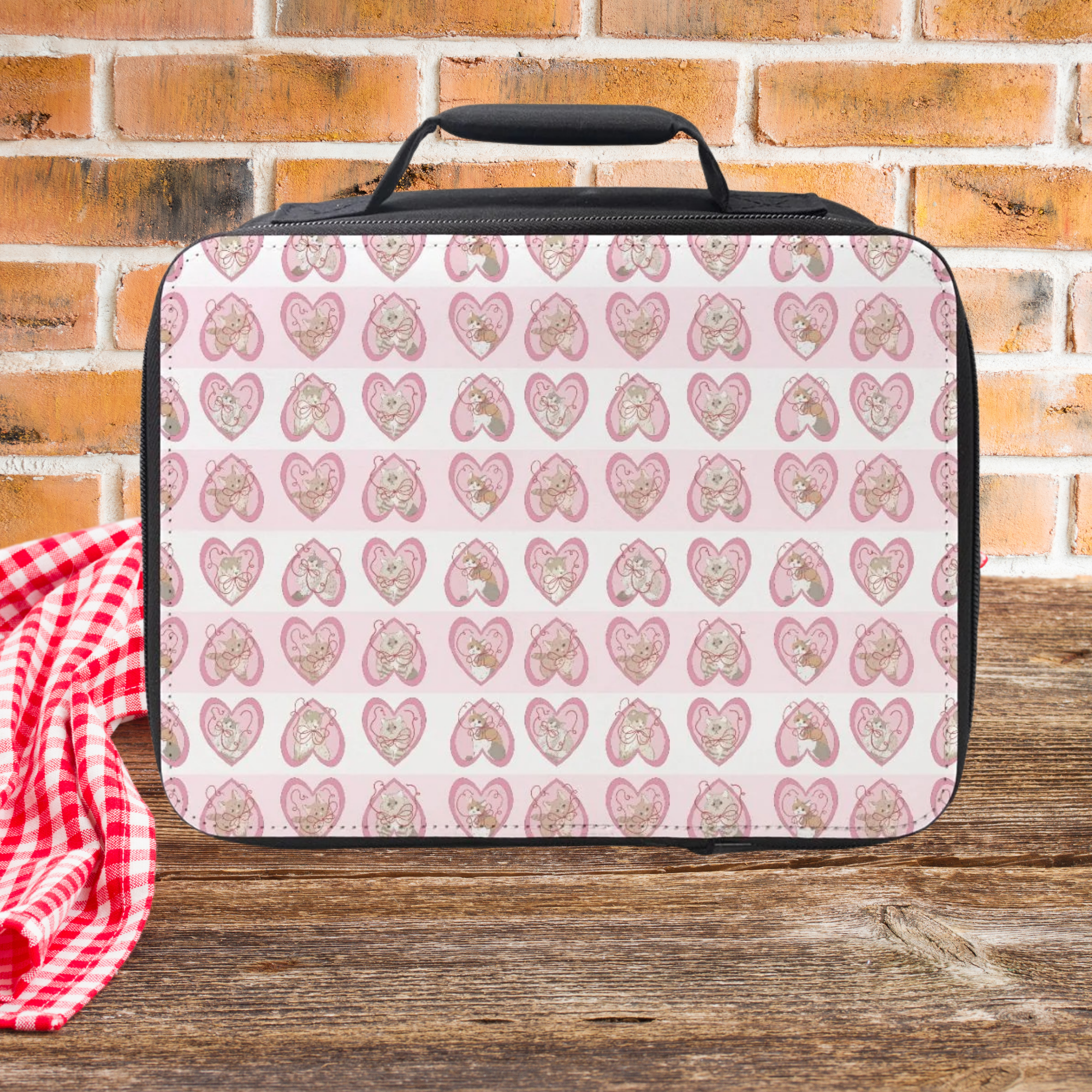 Lunch bag with hand drawn cats in pink hearts pattern on a wooden picnic table with a brick wall background