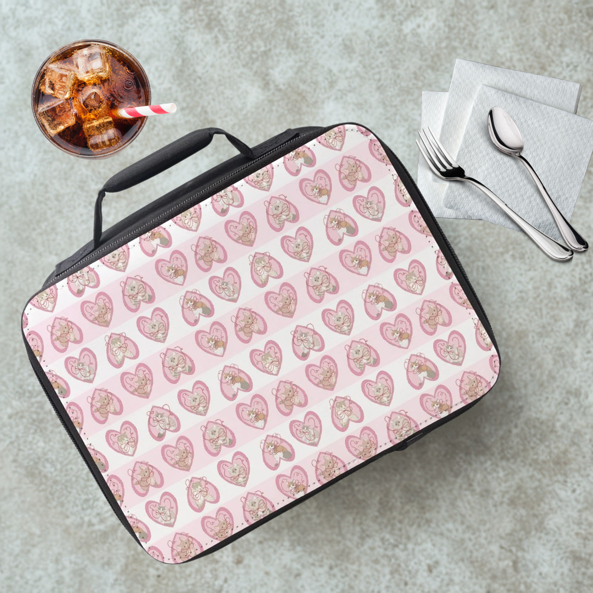 hand drawn cats in pink hearts patterned lunch bag on a cafeteria table with a drink and utensils.