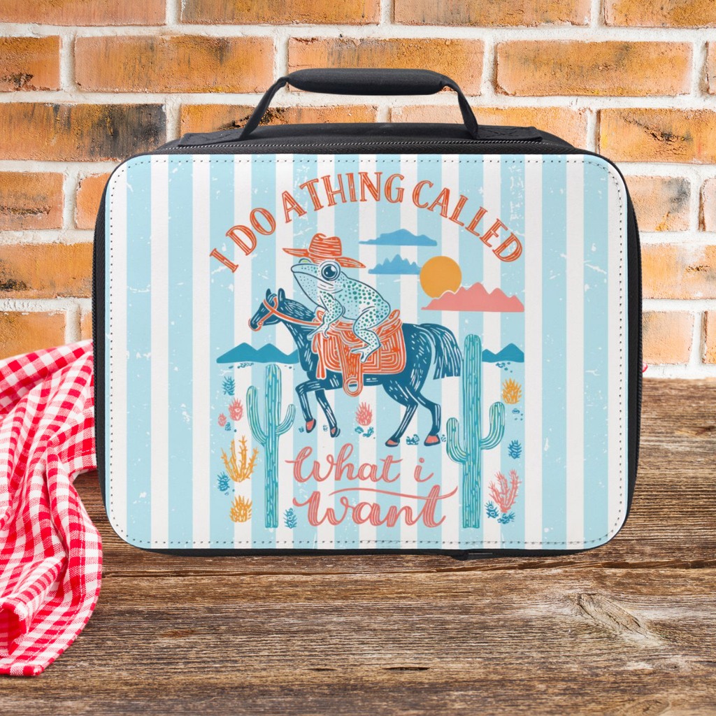 Lunch bag with cowboy frog design and text on a wooden picnic table against a brick wall background