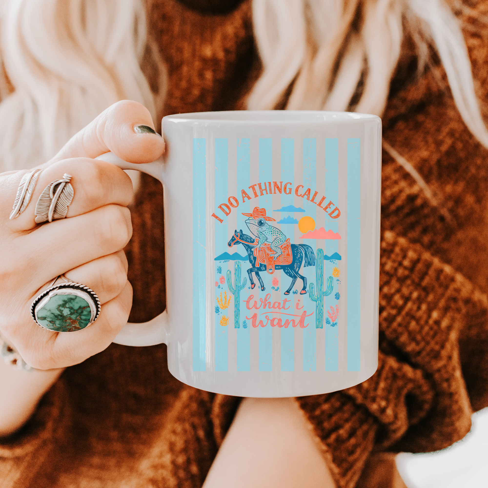 Person holding a 11oz. mug with a colorful design and text, wearing a brown sweater.