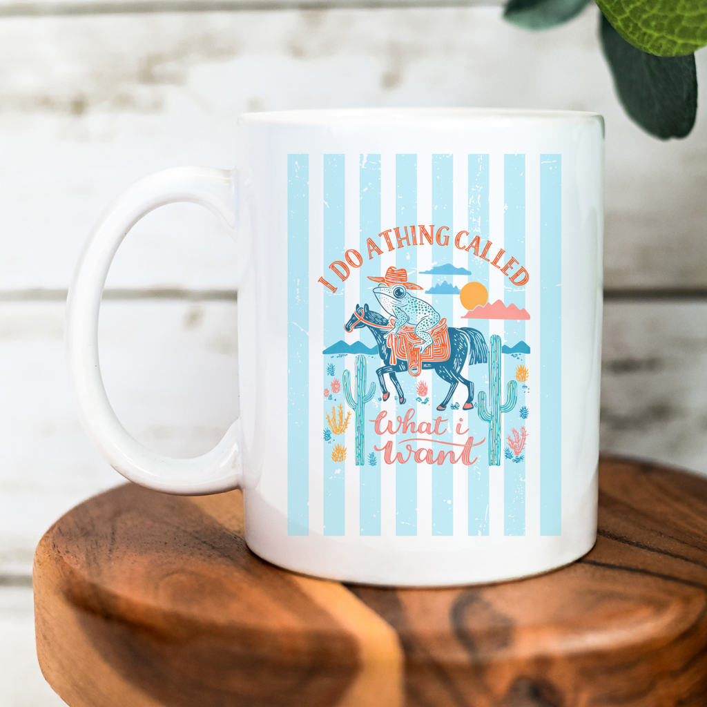 White 11oz. mug with a colorful striped western cowboy frog design featuring a horse and text on a wooden surface.