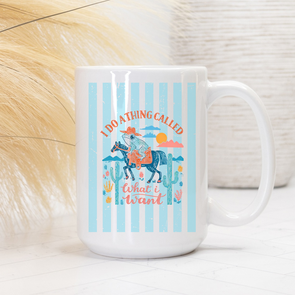 White 15oz. mug with a colorful striped design featuring a cowboy frog on a horse, cacti, and text, set against a textured white and beige background.