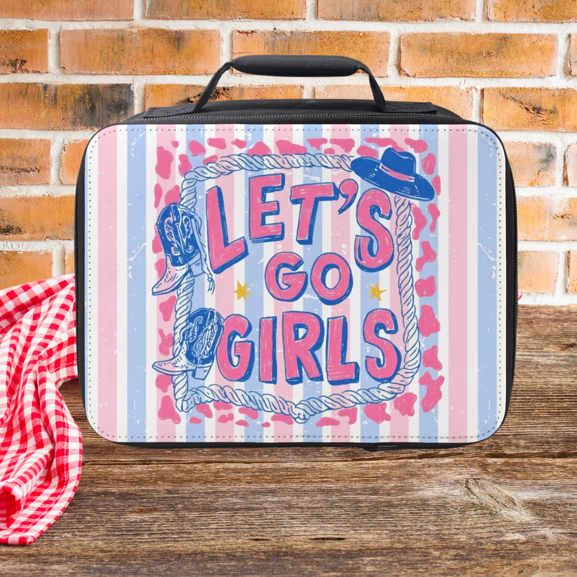  insulated lunch bag with 'Let's Go Girls' text and cowboy hats design on a wooden picnic table and brick wall background