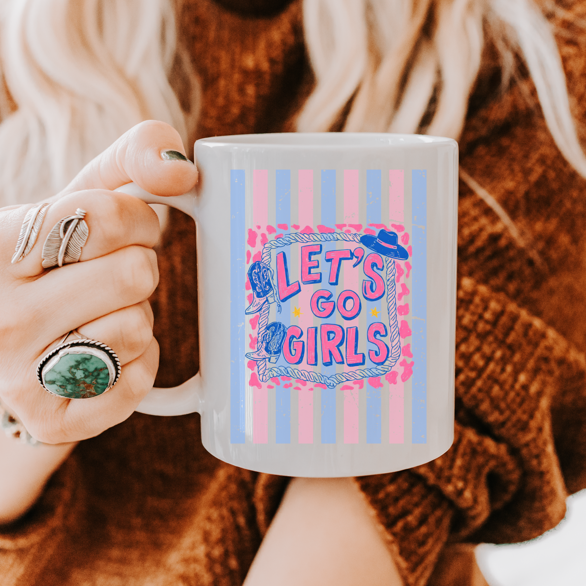 Person holding a 11oz. mug with 'Let's Go Girls' design, wearing a brown sweater and rings.
