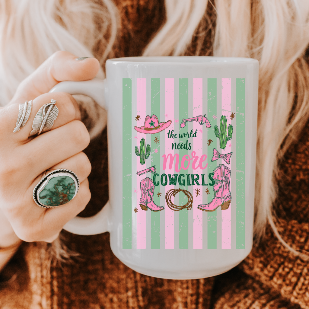 15oz Mug with 'the world needs more cowgirls' design held by a person wearing rings.