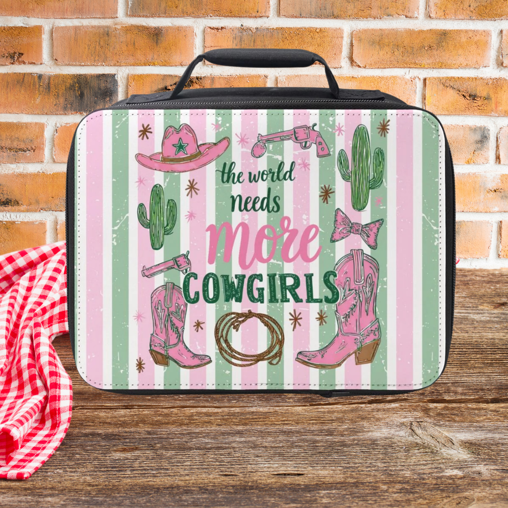 Lunch bag with trendy striped cowgirl-themed design and text 'the world needs more cowgirls' on a wooden picnic table and brick wall background.