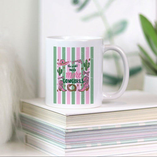 White 11oz mug with pink and green design on a stack of books with plants in the background
